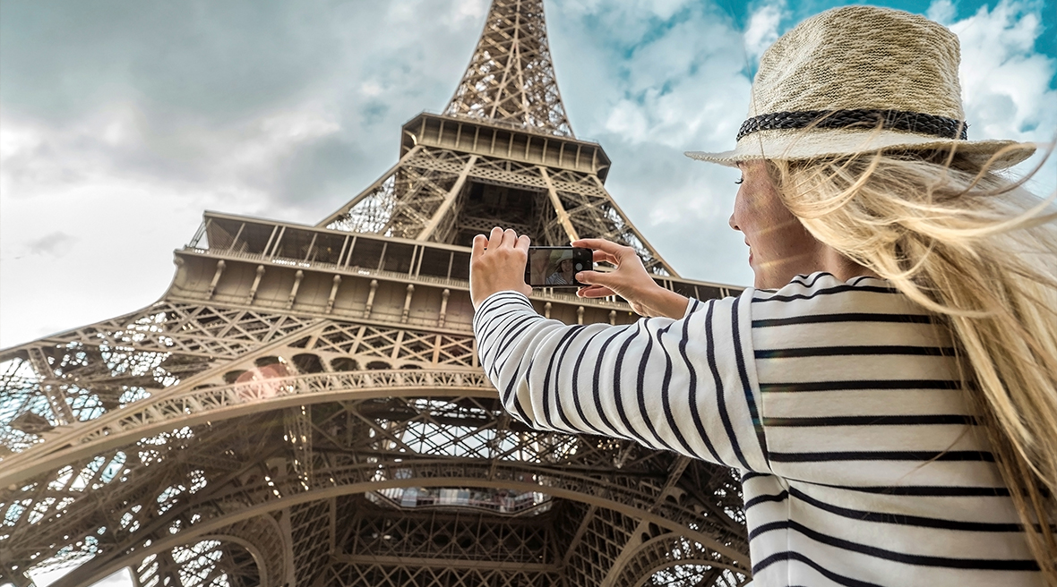Woman tourist in striped top and hat takes picture of Eiffel Tower in Paris under sunlight